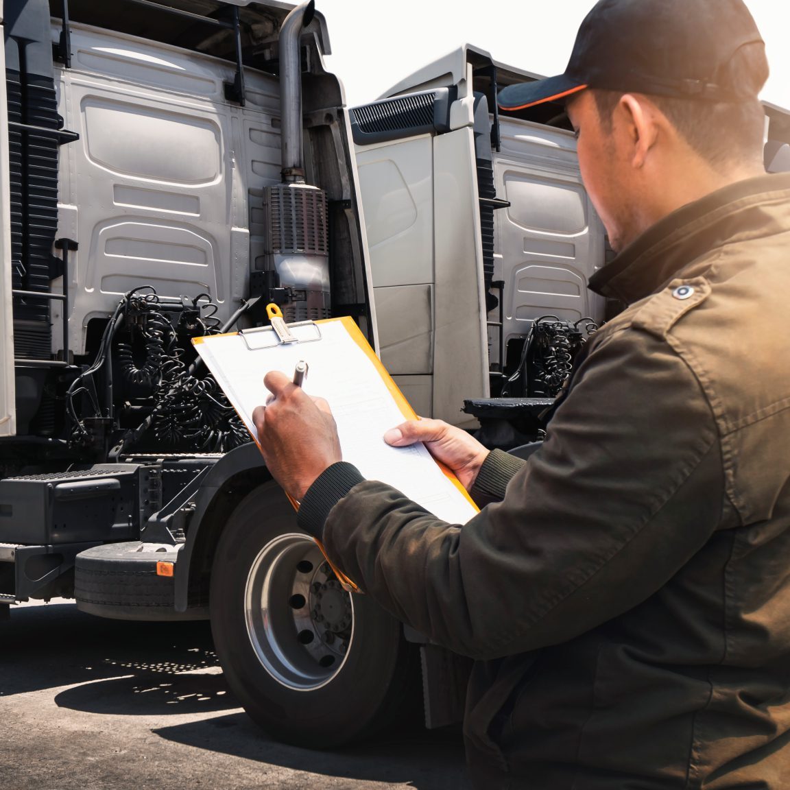 Man inspecting trucks with clipboard, outdoors.